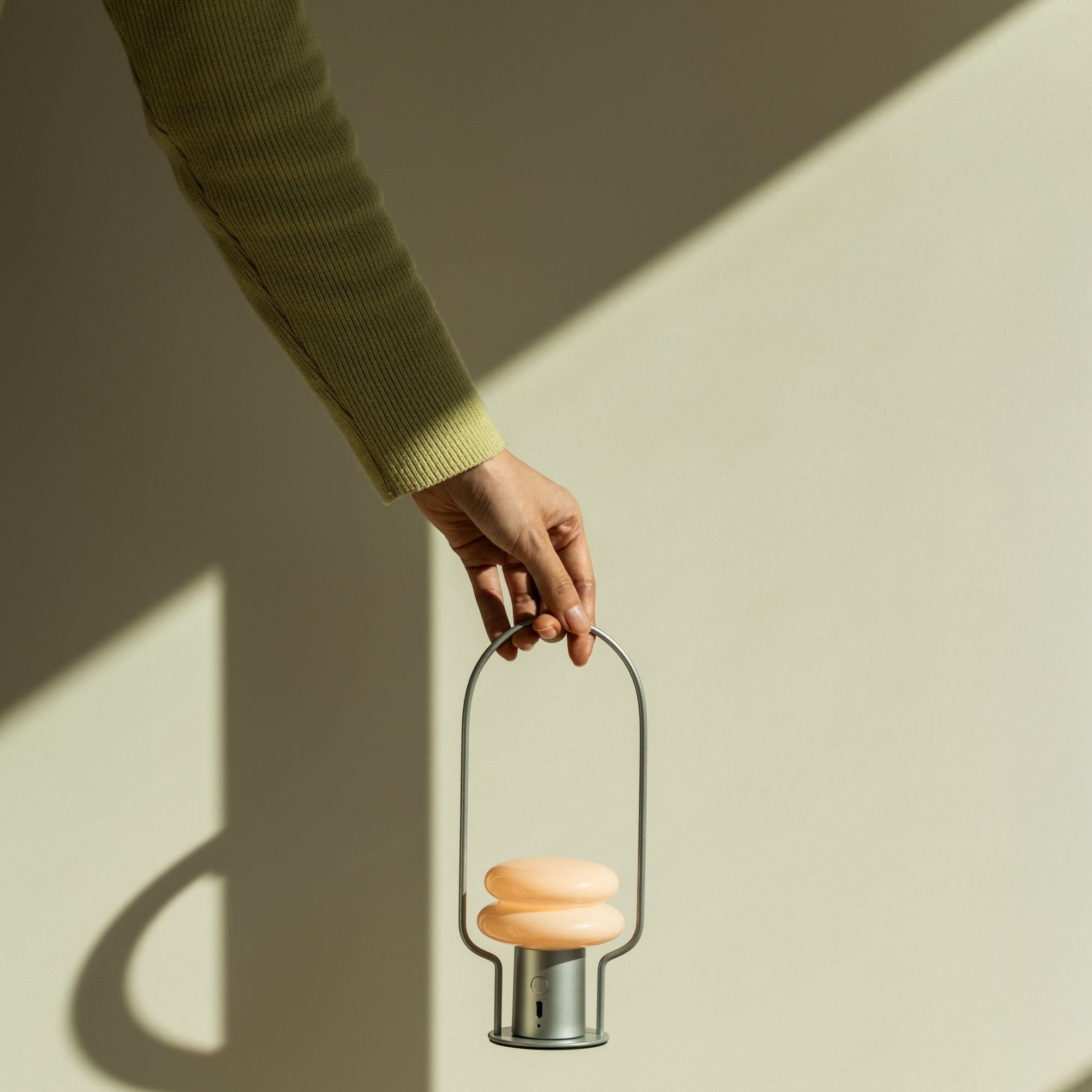 Hand holding a small metal lantern with a light inside against a neutral background