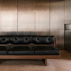 BASSO black leather sofa against a brushed metal wall in a minimalist interior