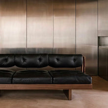 BASSO black leather sofa against a brushed metal wall in a minimalist interior