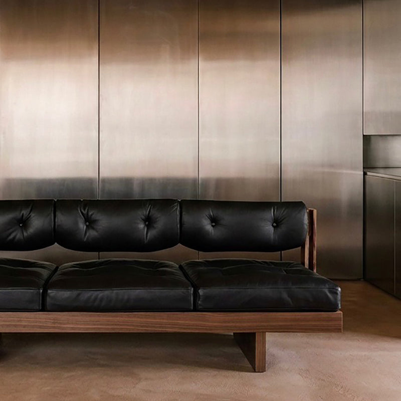 BASSO black leather sofa against a brushed metal wall in a minimalist interior