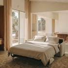 Blossom sofa bed in Bisque, unfolded and styled with cream bedding in a sunlit living room.