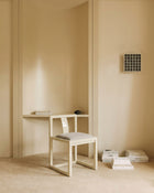 A minimalist cream-colored wooden desk and matching chair with a light gray cushion, styled in a warm, neutral-toned room with beige walls and floor.
