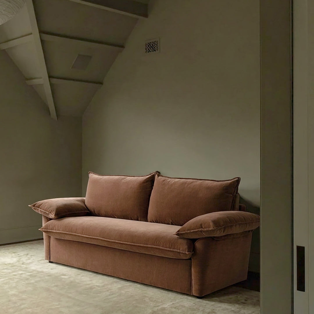 Ease sofa bed in Bronze with cushioned arms and matching back cushions, styled against a warm beige wall.