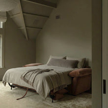 Ease sofa bed in Bronze, unfolded and styled with light bedding in a warm-toned bedroom.