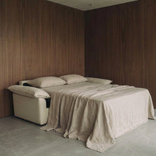 Ease sofa bed in Bisque, unfolded and styled with beige bedding in a wood-panelled room.
