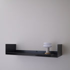 A minimalist black floating wall shelf mounted on a light gray wall, holding a small white mushroom-shaped decorative object.
