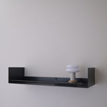 A minimalist black floating wall shelf mounted on a light gray wall, holding a small white mushroom-shaped decorative object.