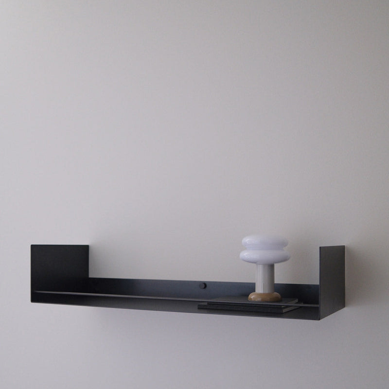 A minimalist black floating wall shelf mounted on a light gray wall, holding a small white mushroom-shaped decorative object.