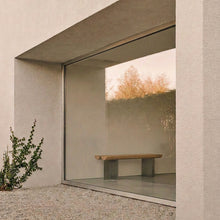 Forma Atelier bench seat in a minimalist interior beside a full-height window overlooking a gravel garden.