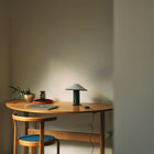 Wooden desk with a lamp, laptop, and chair against a plain wall.