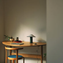 Wooden desk with a lamp, laptop, and chair against a plain wall.