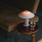 Small wooden side table with a table lamp and glass of water next to a brown  sofa.