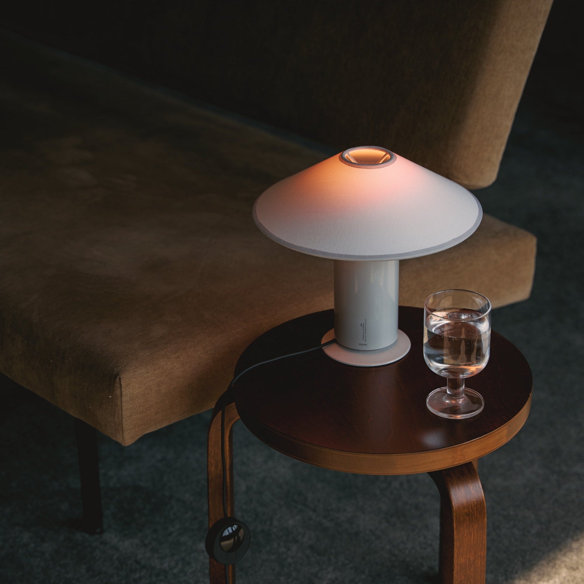 Small wooden side table with a table lamp and glass of water next to a brown  sofa.