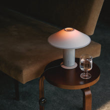 Small wooden side table with a table lamp and glass of water next to a brown  sofa.