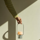 Hand holding a small metal lantern  with a light inside against a neutral background
