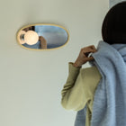 Person holding a light blue scarf in front of an oval mirror with a light fixture.