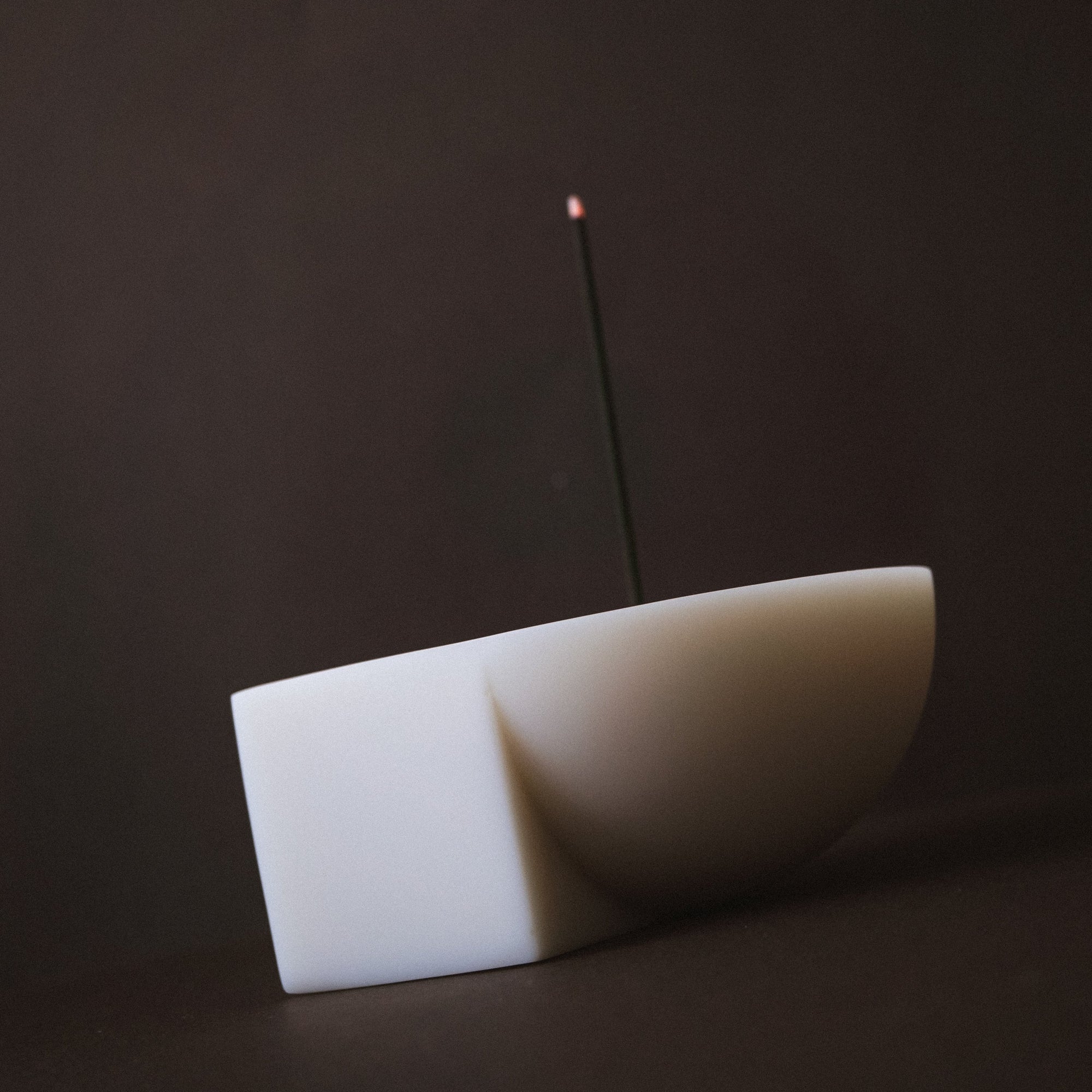Resin incense holder with a single incense stick on a dark background