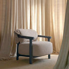 A modern upholstered armchair with a textured light beige fabric and a dark charcoal blue frame, styled in a room with beige curtains and a matching rug.