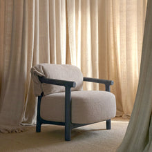 A modern upholstered armchair with a textured light beige fabric and a dark charcoal blue frame, styled in a room with beige curtains and a matching rug.