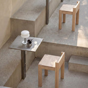 Minimalist outdoor seating featuring light natural wood chairs and square stainless steel tables arranged on concrete steps.