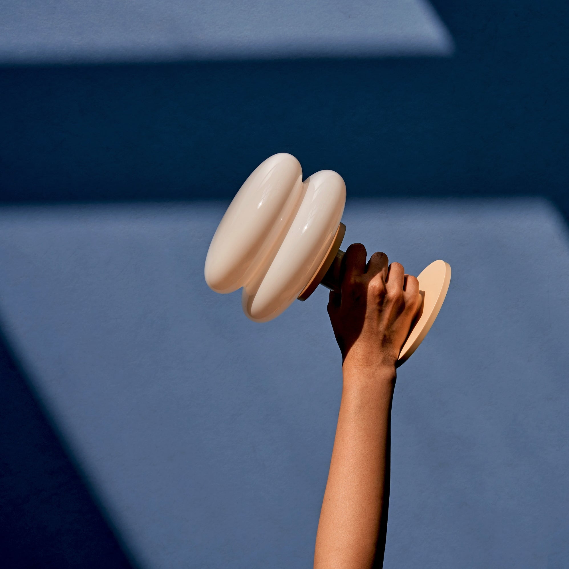 Hand holding a butter and white coloured portable table lamp against a blue background