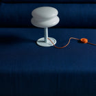 White lamp shade with a pale blue base and an orange cord with a blue sofa in the background