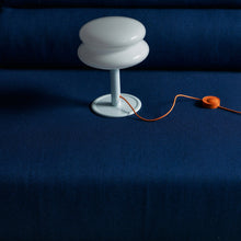 White lamp shade with a pale blue base and an orange cord with a blue sofa in the background