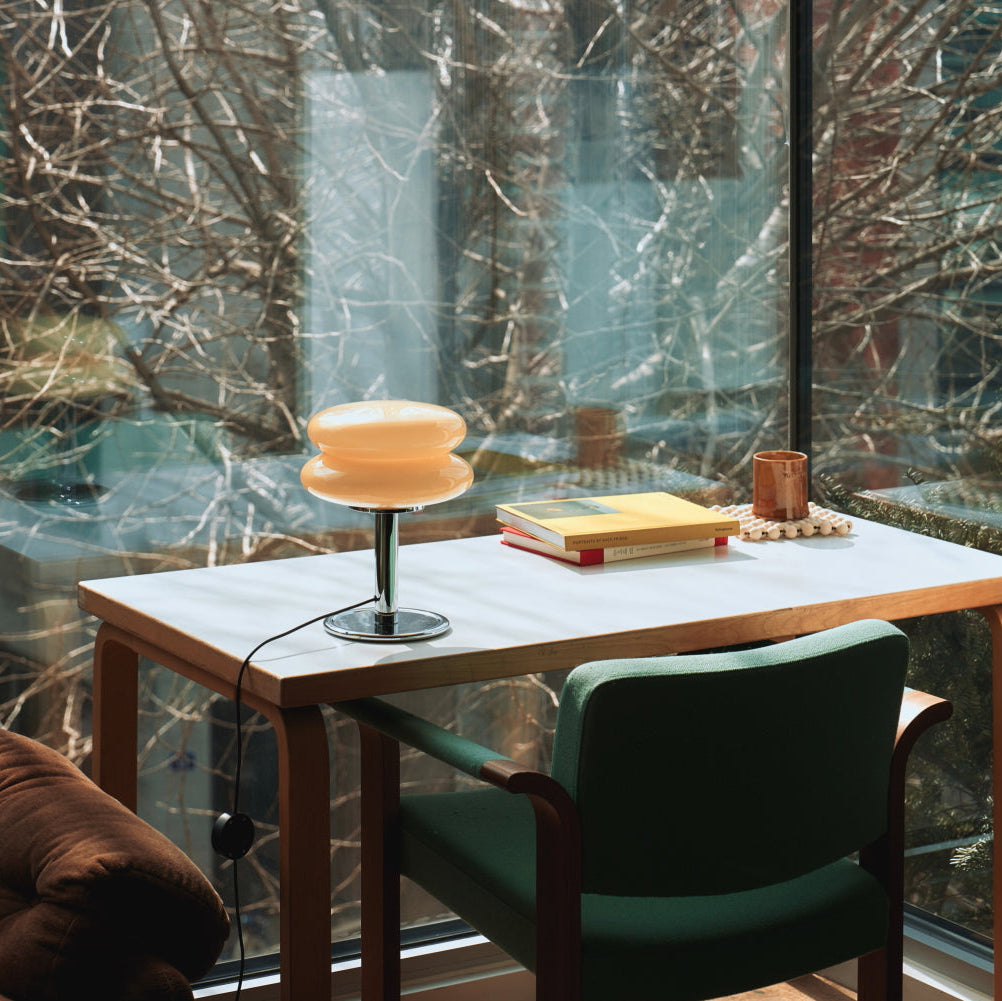 Desk with lamp and books in front of a large window with a snowy landscape.