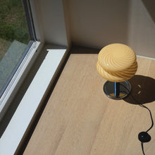 Butter spiral lamp shade on a wooden surface near a window