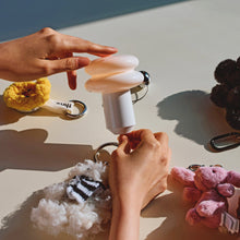 Hands holding a portable lamp with various keychains on a light surface.