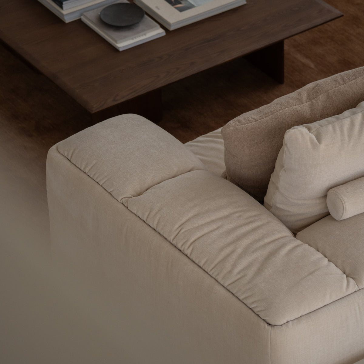 Detail of a cream upholstered sofa with cushions beside a timber coffee table