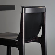Rear close-up of the Burano dining chair in Nero black leather with a black-stained solid ash frame against grey.