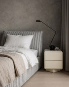 Dormi king single bed in Cloud striped upholstery, styled with neutral bedding beside a cream bedside table.